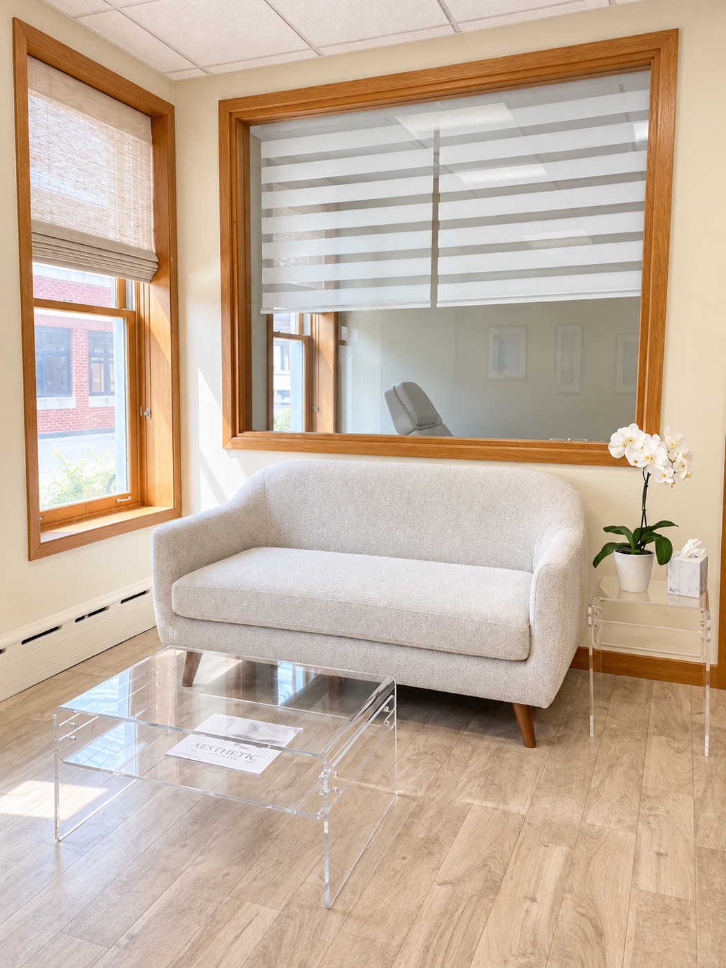 The waiting area with a boucle loveseat beneath a large interior window and a white orchid, where guests gather before an event.